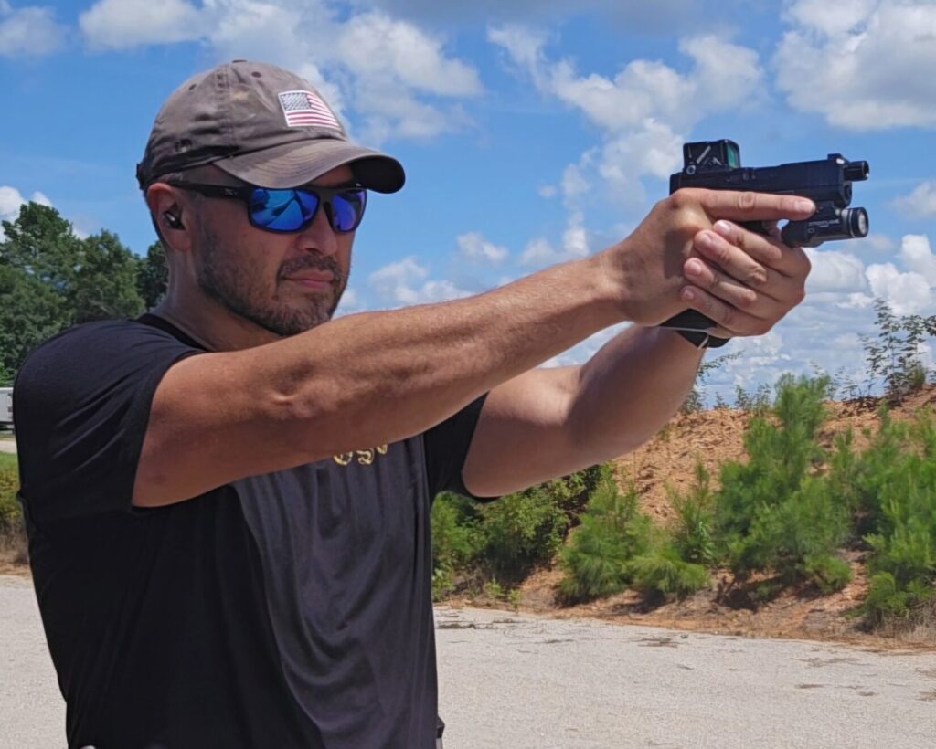 A man in a black t shirt and hat shooting a pistol with two hands.