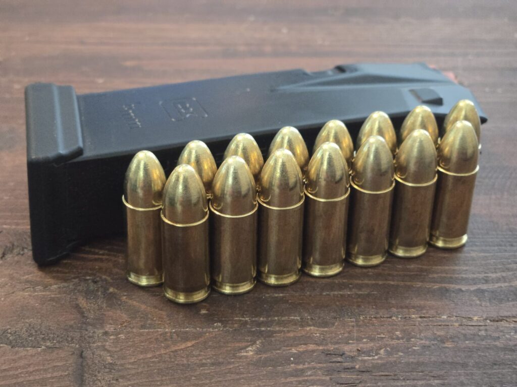 15 rounds of ammunnition and a pistol magazine on a wooden table