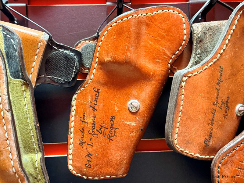 A light brown holster with writing on it that says "Rogers" hanging on a wall.