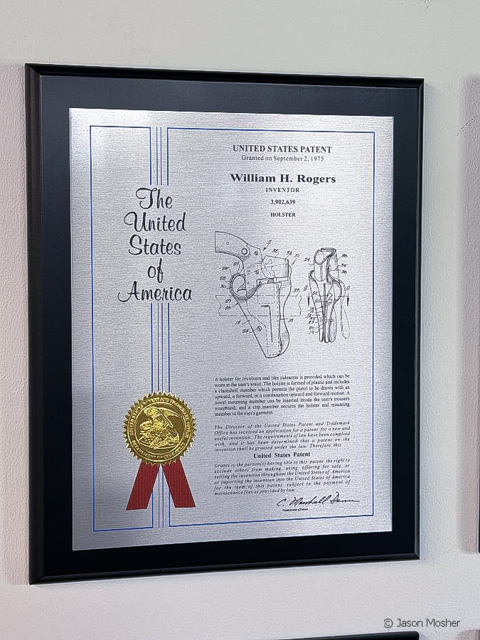 A silver patent certificate in a black frame hanging on a grey wall.
