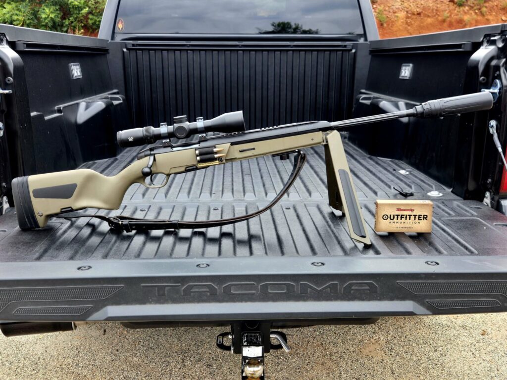 A rifle on top of a pickup truck tailgate with a box of ammuntion