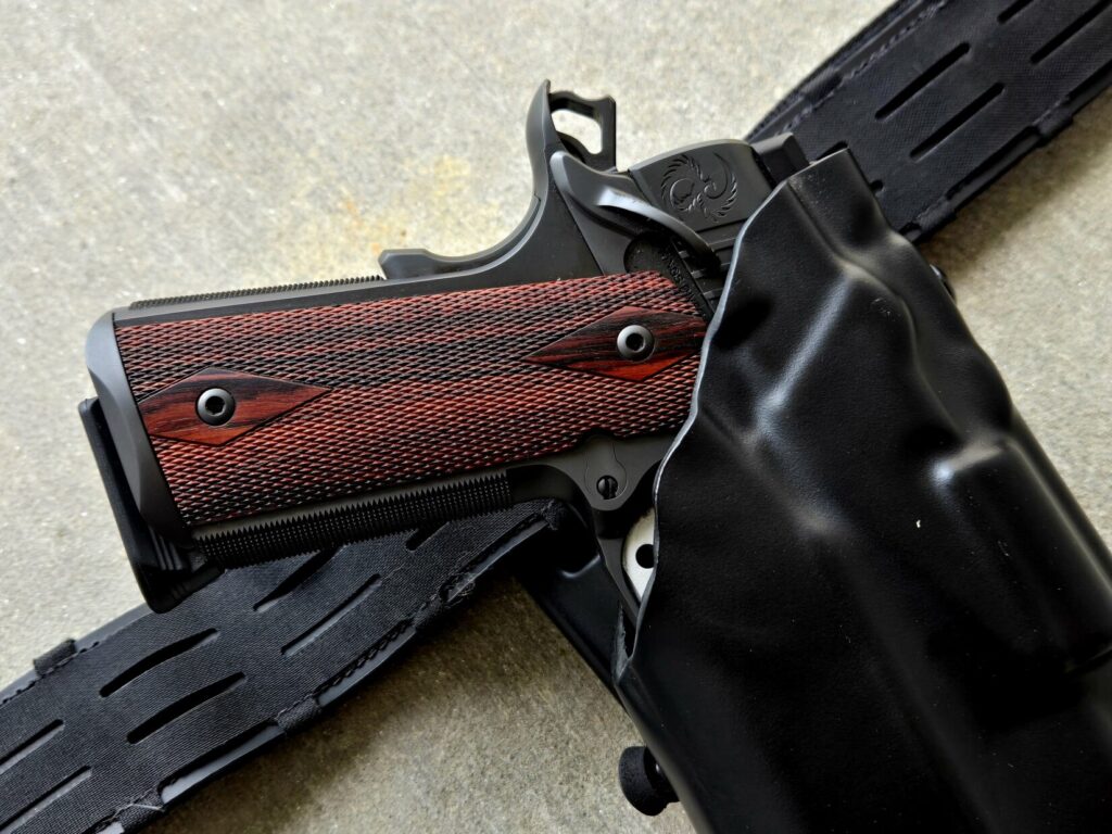 A 1911 Pistol in a holster with cocobolo grips, extended mag well, and cocked hammer.