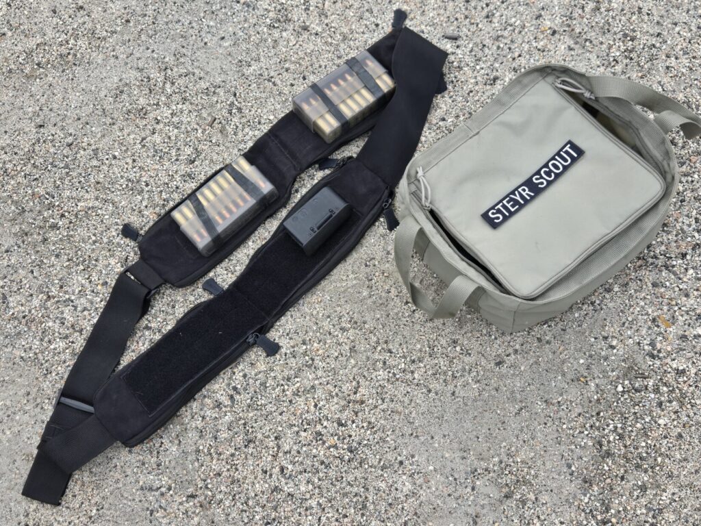 A bandoleer, boxes of ammunition, and bag on a gravel backdrop.