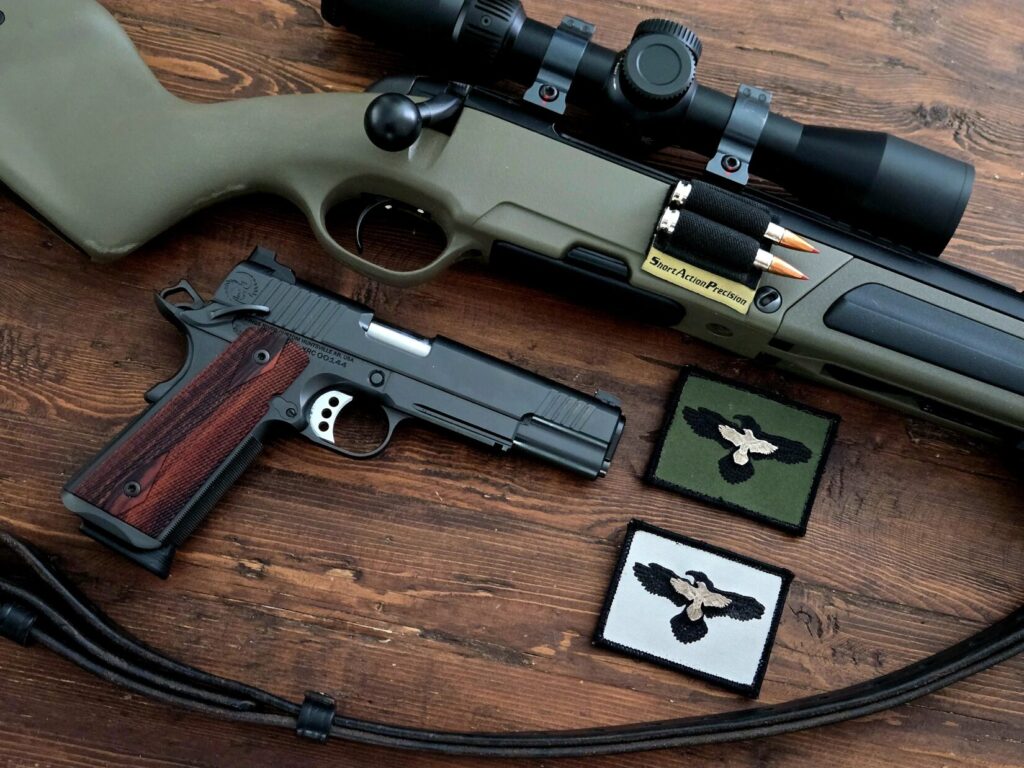 A rifle and a pistol on a wooden table with two patches from GUNSITE