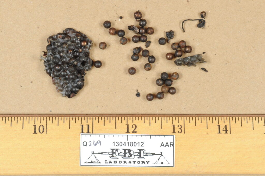 Image of ball bearings and some of the material that held them in a bomb. A ruler is next to the ball bearings. The ruler is marked F B I. This image was a trial exhibit.