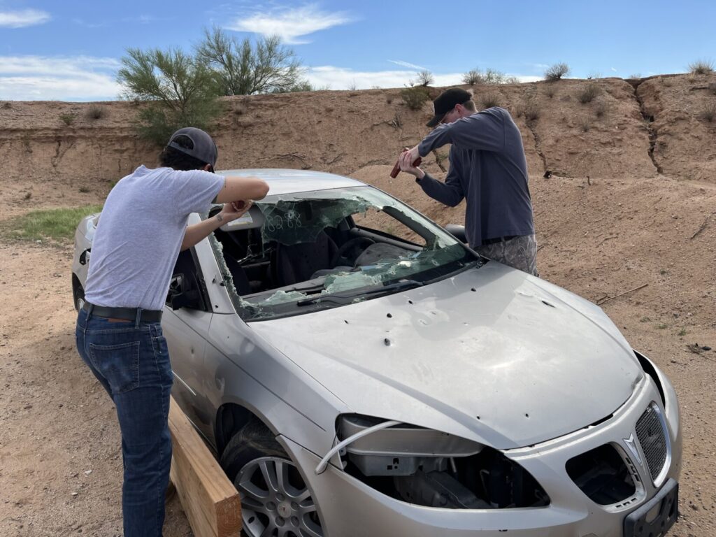 Image of two shooters holding their (plastic replica) pistols above the glass of an automobile to minimize glass fragmentation if it comes to shooting.