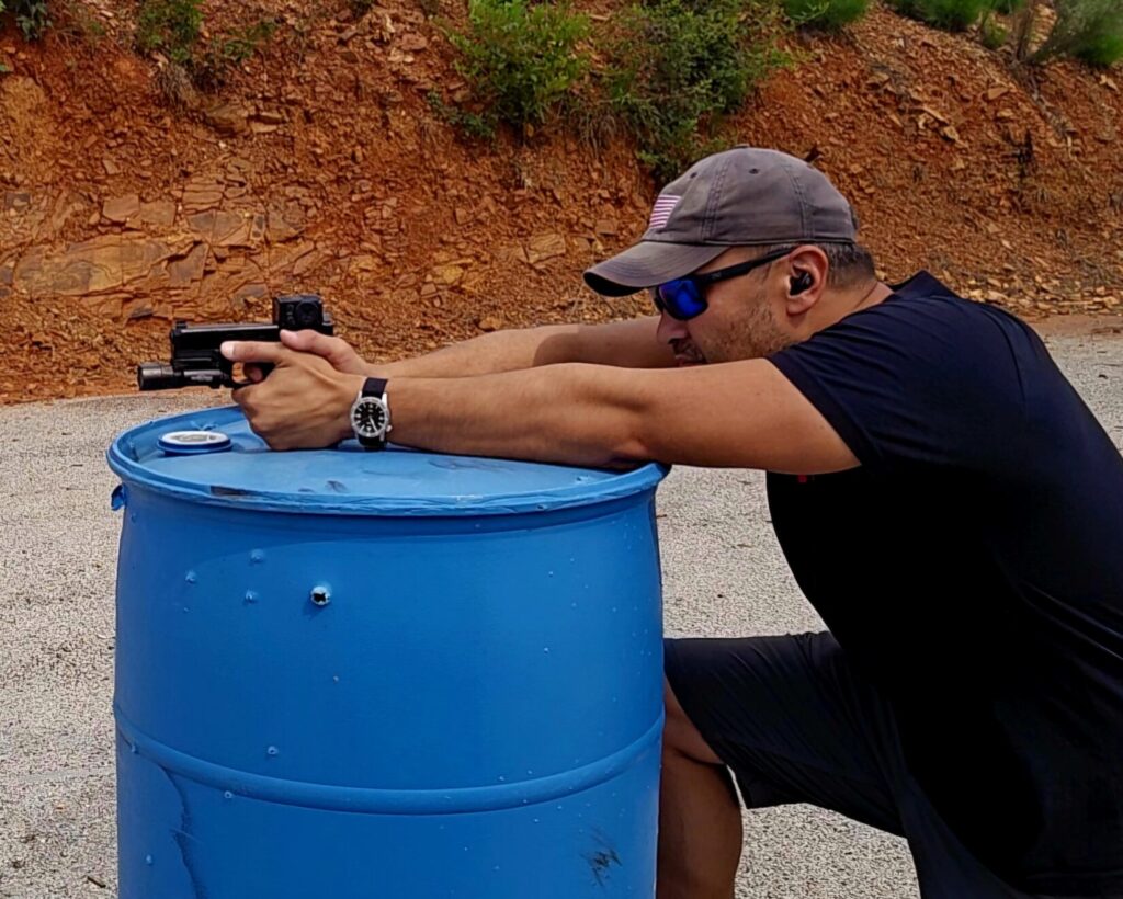 A shooter resting his forearms on a barrel to steady a long-range pistol shot