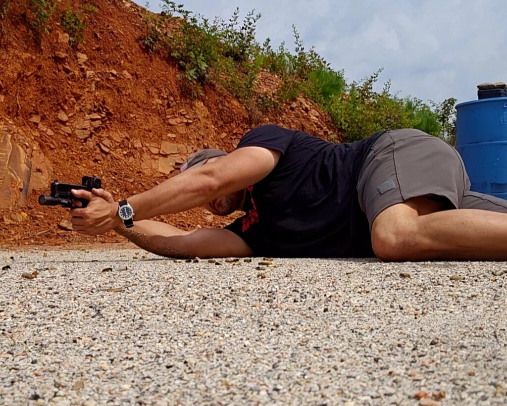 Kevin Estela shooting a pistol from a side-rolled prone variation with one leg drawn up and his torso slightly raised