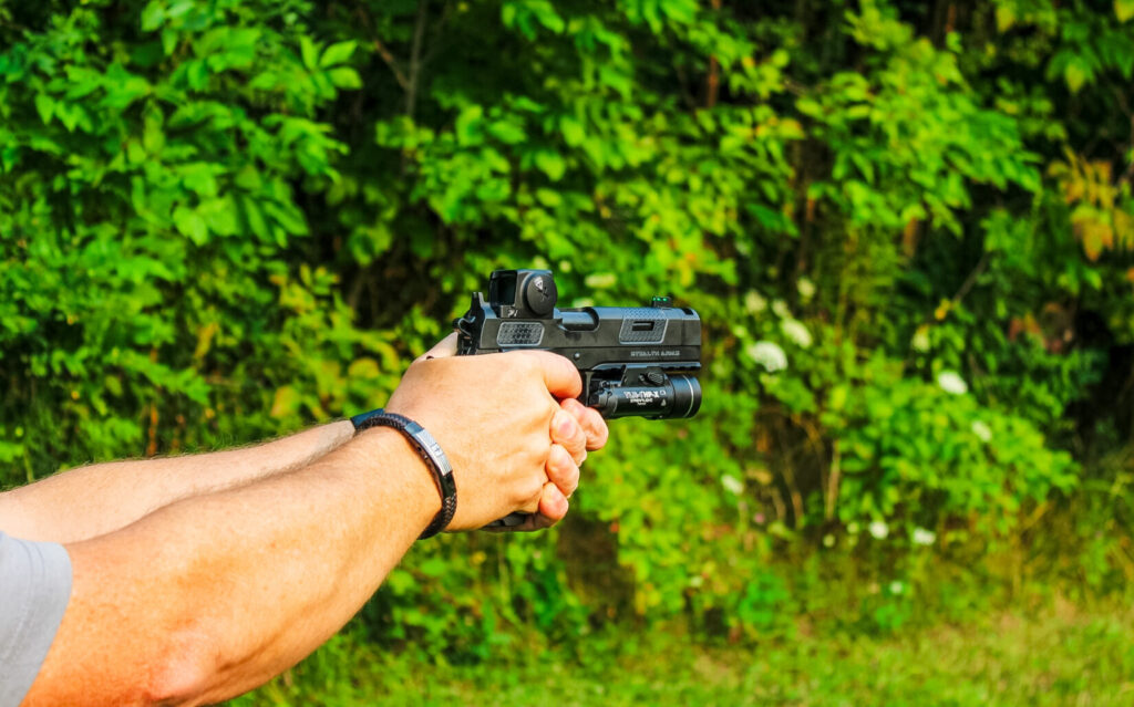Man holding a black pistol on a natural background.