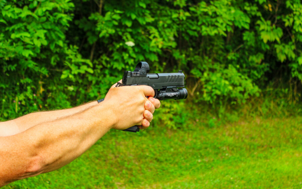 Man holding a black pistol with a natural background.