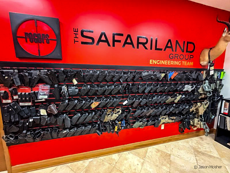 A red wall with black holsters attached to it in rows. The words "Safariland" is printed on the top of the wall in black.
