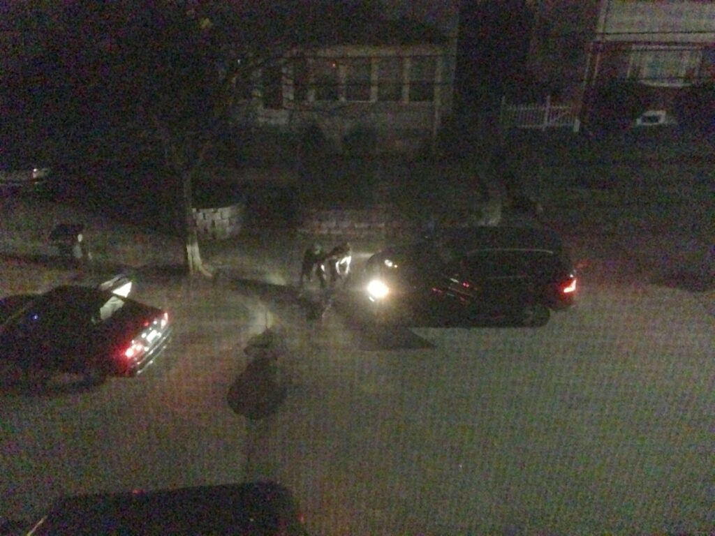 Nightime image to two terrorists in Watertown Massachusetts, taken from an upper floor window of an adjacent house. The image has criss-crossed lines indicating it was filmed through a screen window.