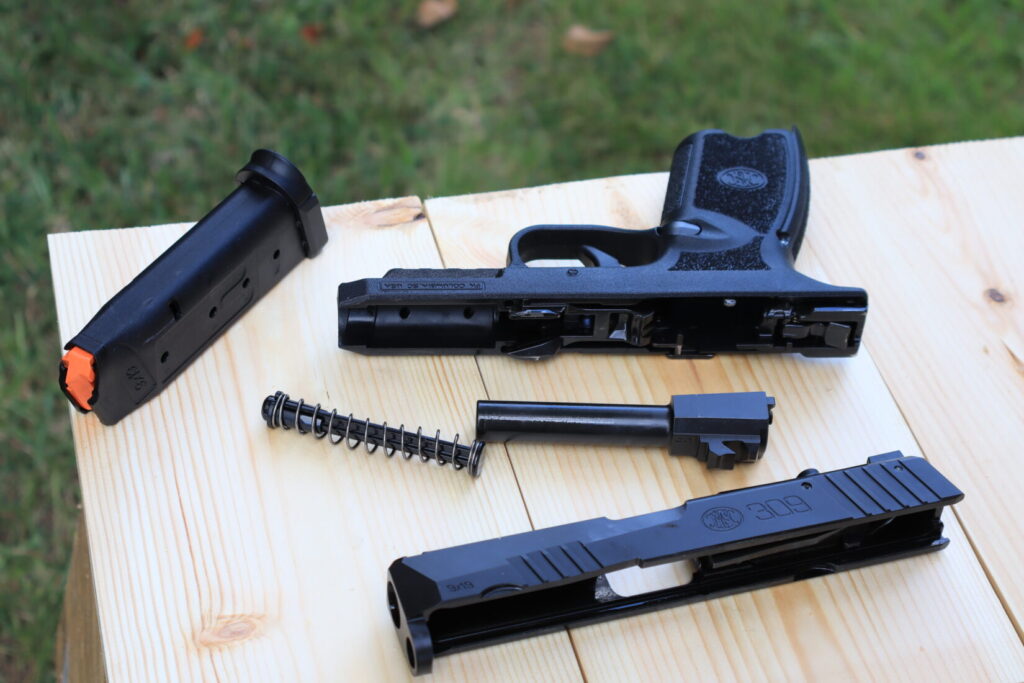 The FN 309 MRD field-stripped into slide, frame, barrel, recoil spring, and magazine, showing the internal hammer at the rear of the frame