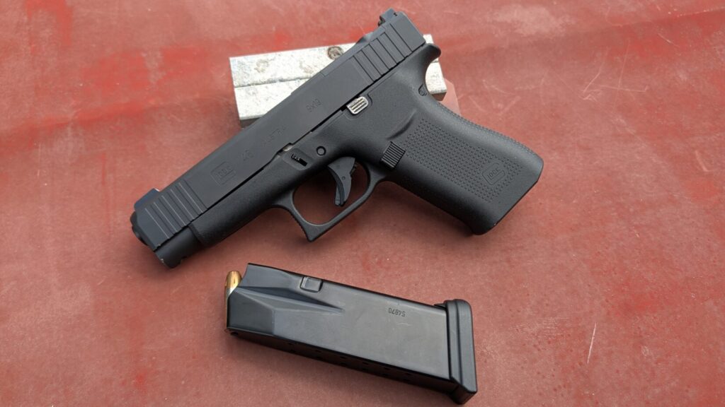 Glock 48 pistol displayed alongside a loaded 15-round magazine on a red surface.