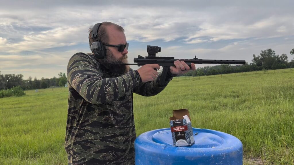 Man in a tiger stripe camo Safariland long-sleeve hoodie aiming a rifle at an outdoor range.