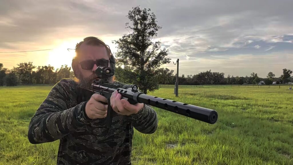Front-facing view of a man aiming a rifle downrange while wearing the tiger stripe camo hoodie.