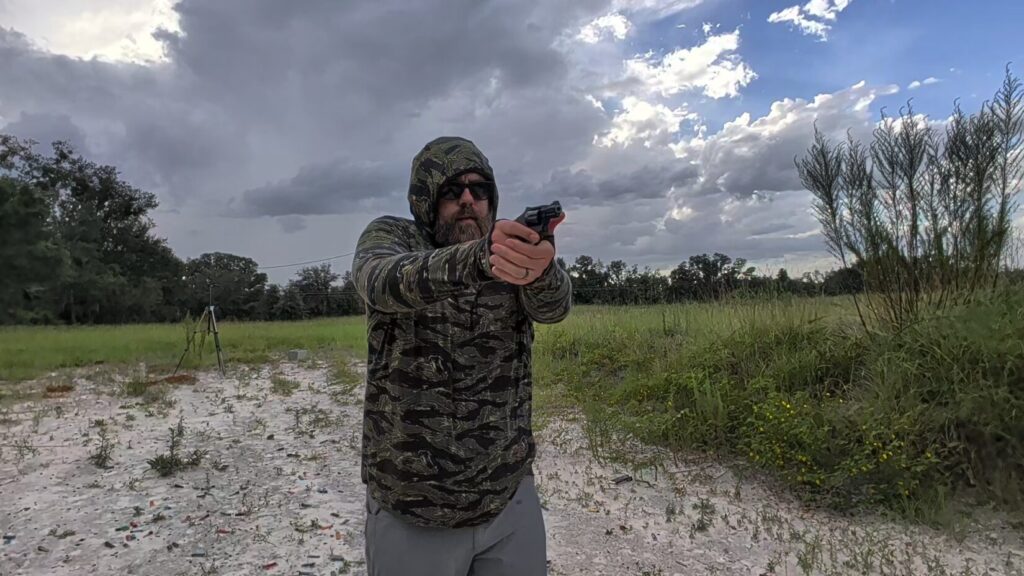 Man with hood raised wearing the tiger stripe camo Safariland hoodie aiming a revolver.