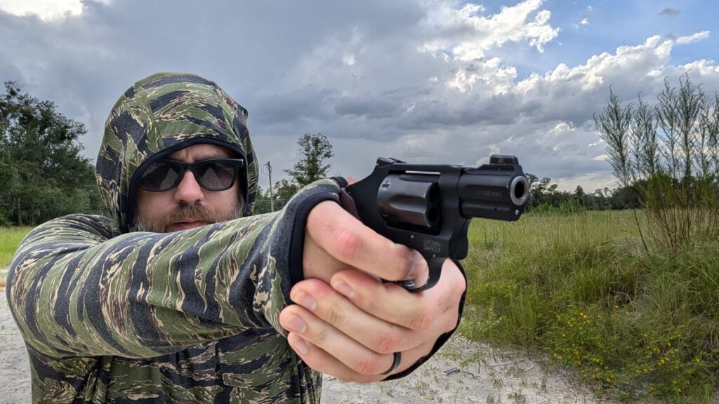 Close-up front view of a man with hood up aiming a small revolver directly forward.