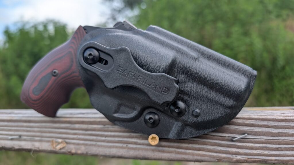 Wide side-view shot of the J-frame revolver secured in a black Safariland holster on an outdoor wooden rail.