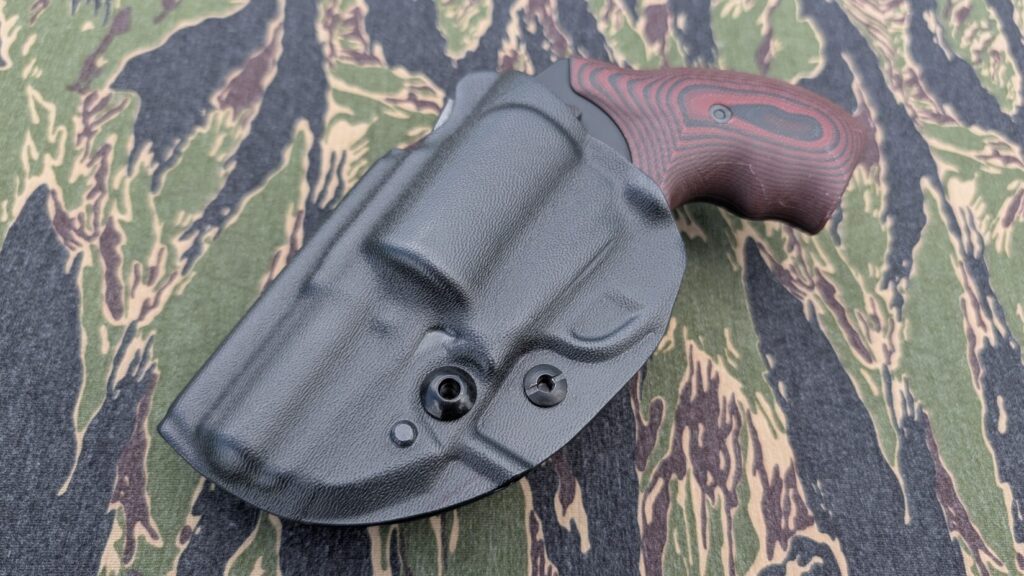 Overhead flat-lay view of a holstered J-frame revolver centered on tiger-stripe camouflage fabric.