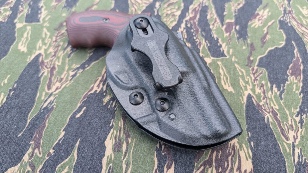 Back shell of a black revolver holster showing attachment points, resting on tiger-stripe camouflage material.