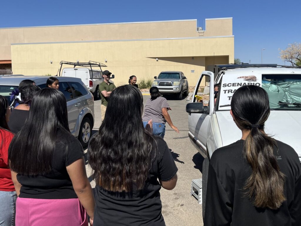 Several Personal Protection students observe a student running to the back of a white GMC Yukon when threatened by an instructor with a yellow plastic replica pistol.