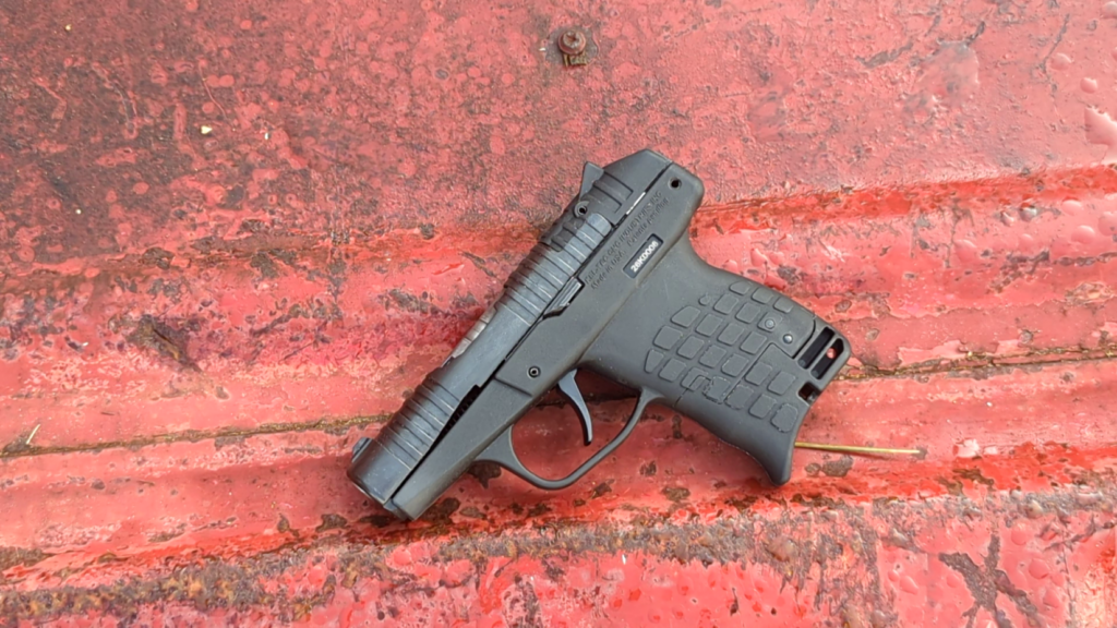 Right-side profile of a compact black PR-3AT pistol displayed against a weathered, red painted surface