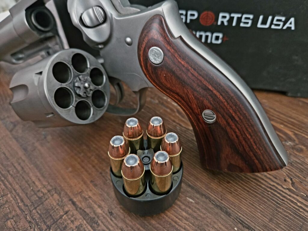 A revolver, a speed loader, and an ammo container on a wooden backdrop