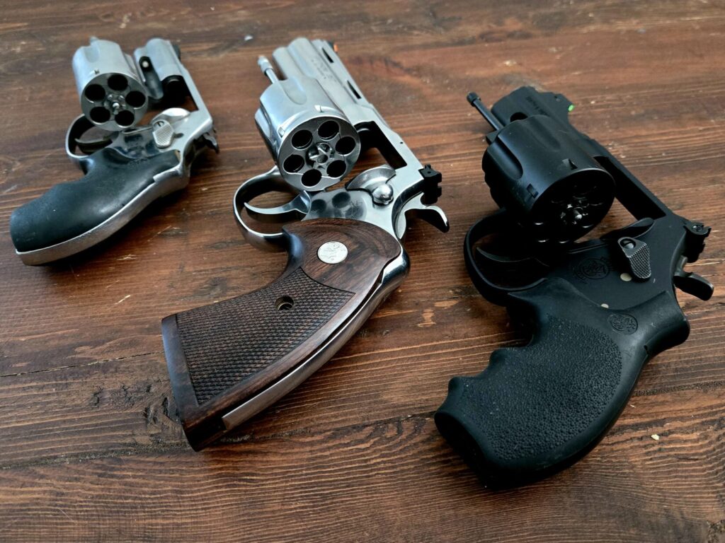 A Smith & Wesson J Frame, Colt Python, and Smith & Wesson Night Guard on a wooden backdrop