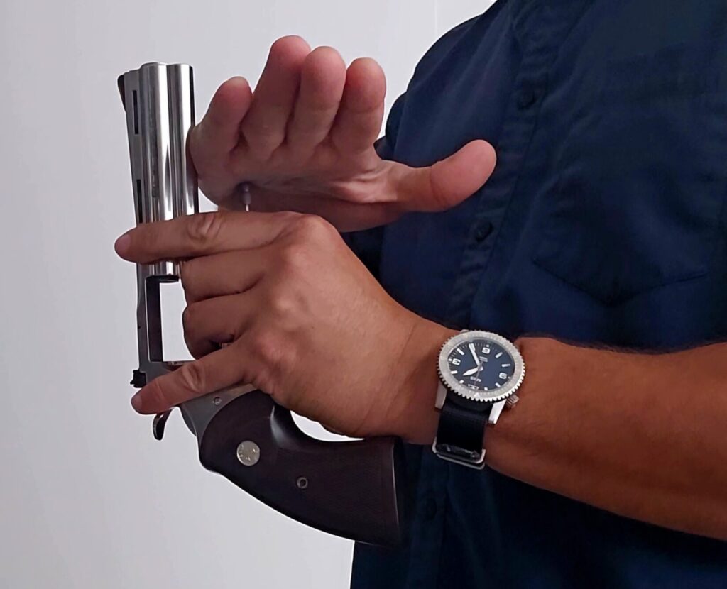 A man holds a stainless revolver upside down and pushes on the ejector rod to clear spet casings.