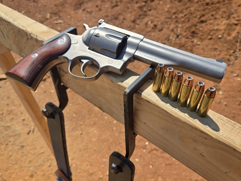 The Ruger Redhawk resting on a target stand next to six rounds of hollow point ammunition
