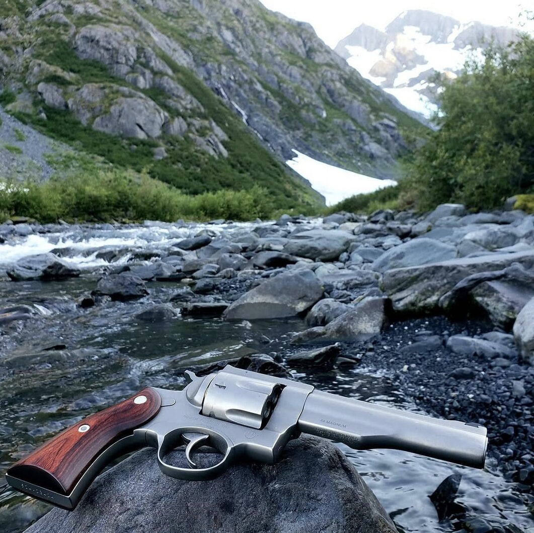 The custom Ruger NP3 Redhawk resting on a rock with an Alaska mountain and river backdrop