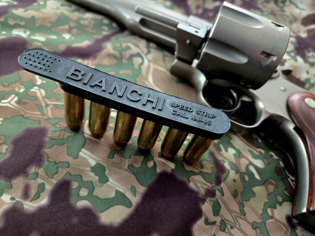 A Bianchi speed strip loaded with six rounds, resting on a Kryptek-pattern background