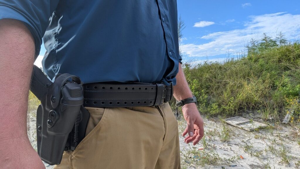 A person wearing Safariland HOLLE belt with a black handgun holster mounted on the right hip and canted away from the body.