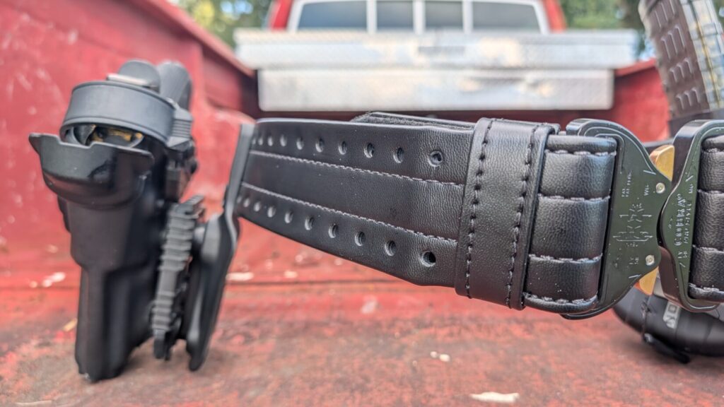 Angled close-up of a Safariland HOLLE belt showing its mounting holes, stitching, and an attached holster