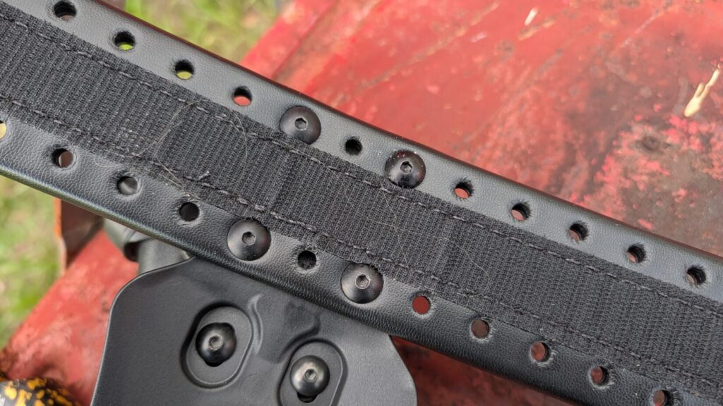 A close-up of the inner side of a black HOLLE belt, showing a central strip of Velcro and black screws securing an attachment.