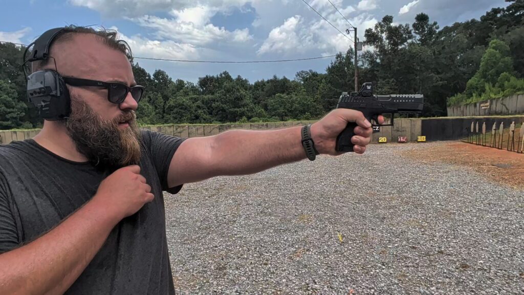 Travis Pike firing a CZ DUTY left-handed at the Range Ready outdoor range, with an ejected casing flying above the gun