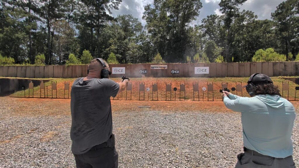 Two shooters firing handguns at multiple targets on an outdoor range lined with CZ banners during a Trident Concepts class
