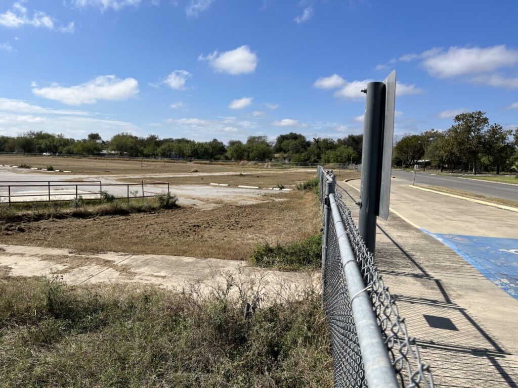 Image of an untended playground at Robb Elementary School. There is a treeline on the other side of a canal about 100 yards away.