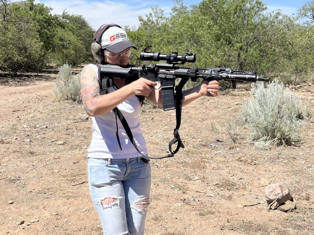 A woman shoots a rifle from the shoulder while walking across a firing range.