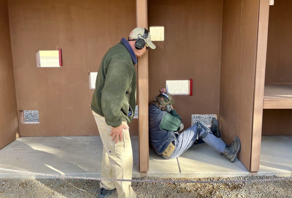 Steve Rodriguez, a retired Albuquerque P. D. SWAT sniper, coaches a student shooting a rifle through irregularly placed holes in a wall at Thunder Ranch, a shooting school in Oregon.
