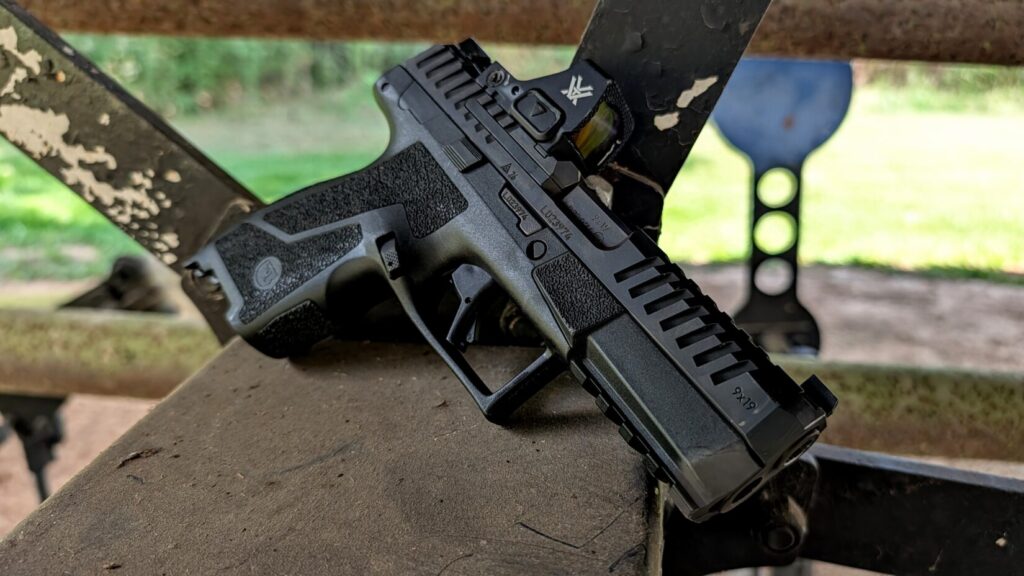 Black CZ DUTY 9mm pistol with a Vortex red dot sight resting on a weathered metal structure outdoors